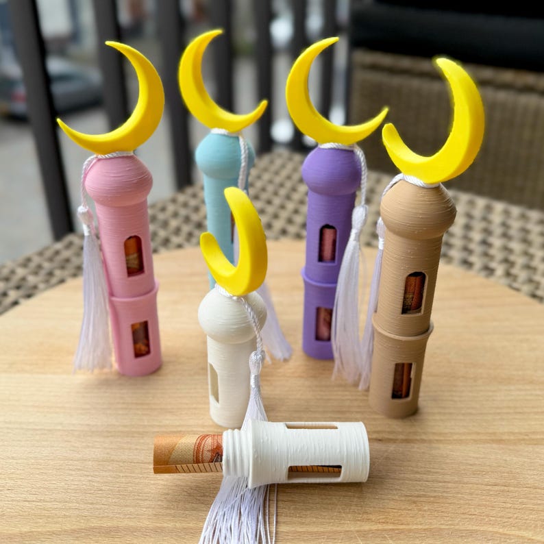 May include: Five colorful decorative towers with crescent moon tops and white tassels. The towers are made of plastic and have a clear window to see inside. One tower is white and has a bill inside.