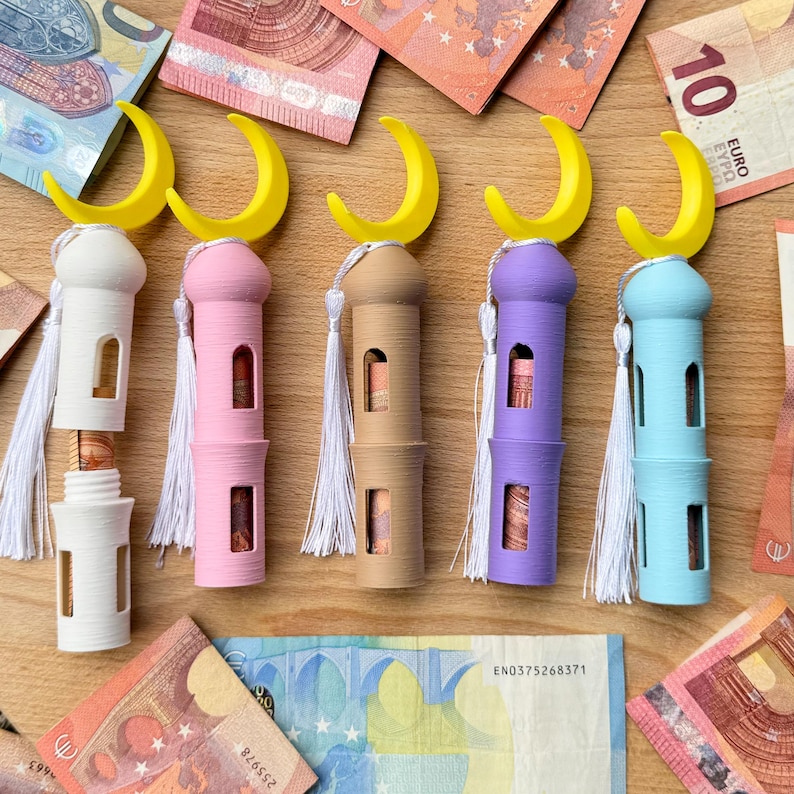 May include: Five decorative containers shaped like mosques with crescent moon tops. The containers are in white, pink, beige, purple, and light blue. Each container has a white tassel hanging from the top.