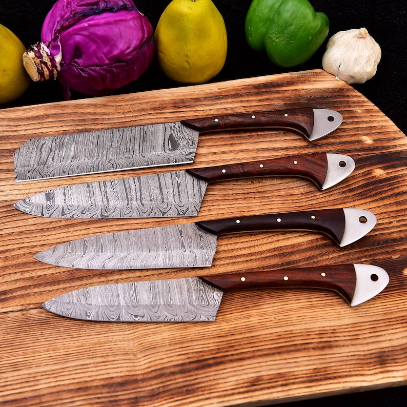 May include: Four Damascus steel kitchen knives with wooden handles on a wooden cutting board. The knives have a wavy pattern and are arranged in a row from largest to smallest.