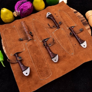 May include: A brown leather knife roll with five slots for knives. The roll is open and five knives with wooden handles are visible. The knives have silver blades.