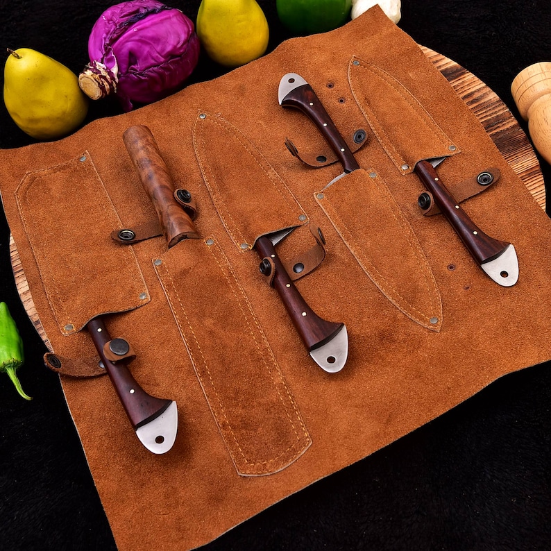 May include: A brown leather knife roll with five slots for knives. The roll is open and five knives with wooden handles are visible. The knives have silver blades.