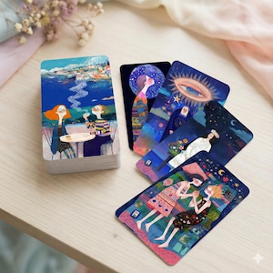 Puede incluir: Una baraja de cartas de tarot ilustradas con obras de arte coloridas. Las cartas representan varias escenas, incluyendo figuras en un café, cuerpos celestes y figuras oníricas. La baraja está apilada sobre una superficie de madera clara.