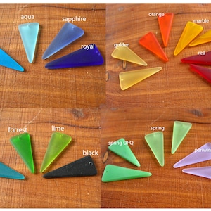 May include: A collection of colorful, triangular pendants in various shades, including blue, green, orange, yellow, red, and purple. Each pendant has a small hole for stringing. The pendants are arranged on a wooden surface.