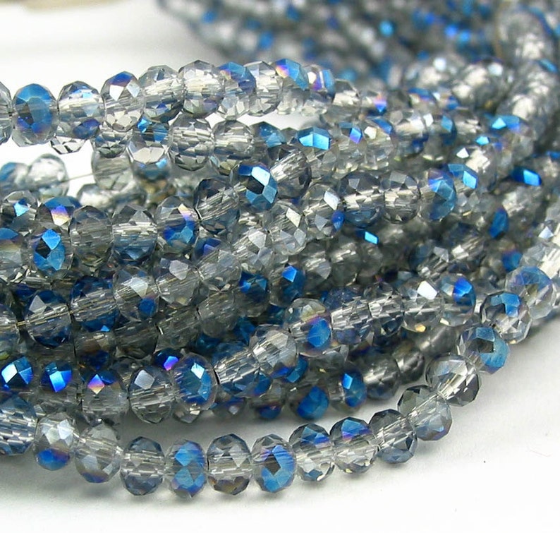 May include: A strand of faceted glass beads in shades of clear and blue. The beads have an iridescent finish, creating a shimmering effect.