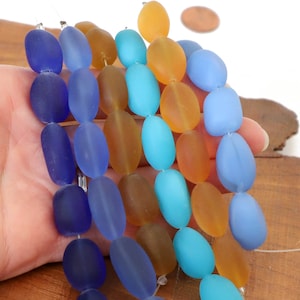May include: A strand of oval-shaped glass beads in shades of blue and amber. The beads are frosted and have a matte finish.