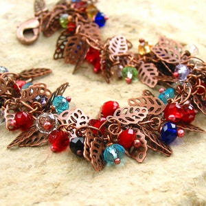 May include: A copper bracelet with a leaf design and colorful beads. The beads are red, blue, green, and clear. The bracelet is made of copper wire and has a delicate, feminine look.