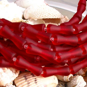K&ouml;nnte beinhalten: Eine Str&auml;hne roter Glasperlen, jede Perle ist in Form einer kleinen Flasche mit abgerundetem Oberteil und leicht ausgestelltem Boden geformt. Die Perlen sind in einem lockeren Haufen angeordnet, wobei sich einige Perlen &uuml;berlappen.