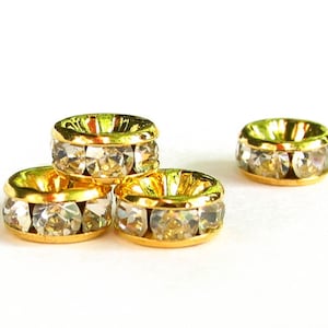 May include: Three gold-toned rings with clear rhinestones set around the edge. The rings are stacked on top of each other.