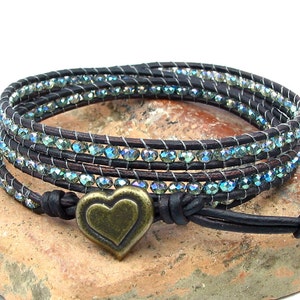 May include: A brown leather wrap bracelet with a heart-shaped charm. The bracelet is adorned with iridescent blue beads.