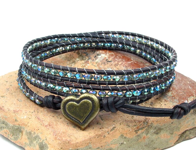 May include: A brown leather wrap bracelet with a heart-shaped charm. The bracelet is adorned with iridescent blue beads.