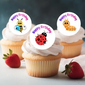Può includere: Tre cupcakes con glassa bianca e decorazioni commestibili. Le decorazioni presentano un'ape, una coccinella e un bruco, ognuno con la scritta "Happy Birthday" in un design circolare. Fragole fresche sono posizionate vicino ai cupcakes.