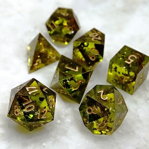 May include: Set of seven green dice with gold numbers. The dice are translucent and have a speckled appearance. The dice are numbered 1 through 6 and 10, 12.