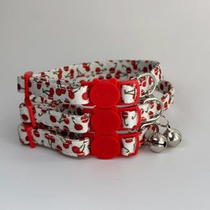 May include: Three white and red cherry print cat collars with red safety breakaway buckles and silver bells.