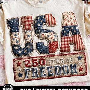 May include: Cream-colored t-shirt with the word "USA" in a patchwork design featuring red, white, and blue patterns. Below, a rectangular emblem reads "250 YEAR OF FREEDOM" with star accents, celebrating a patriotic theme.
