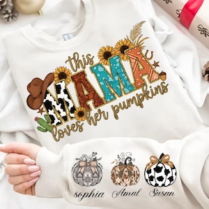 Puede incluir: Sudadera blanca con el texto "this MAMA loves her pumpkins" en un diseño colorido. El diseño incluye girasoles, un sombrero de vaquero y una herradura. Debajo hay tres ilustraciones de calabazas con nombres.