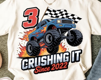 May include: Cream t-shirt with a blue monster truck design, flames, and a checkered flag. The number 3 is prominent, with the text "CRUSHING IT Since 2022" below. A birthday-themed graphic tee.