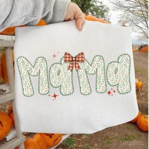 Pode incluir: Toalha decorativa branca com a palavra "Mama" em um design floral com um la&ccedil;o xadrez vermelho e branco. As letras s&atilde;o preenchidas com um padr&atilde;o floral verde e branco e contornadas em verde. Acentos de estrelas vermelhas tamb&eacute;m est&atilde;o inclu&iacute;dos.