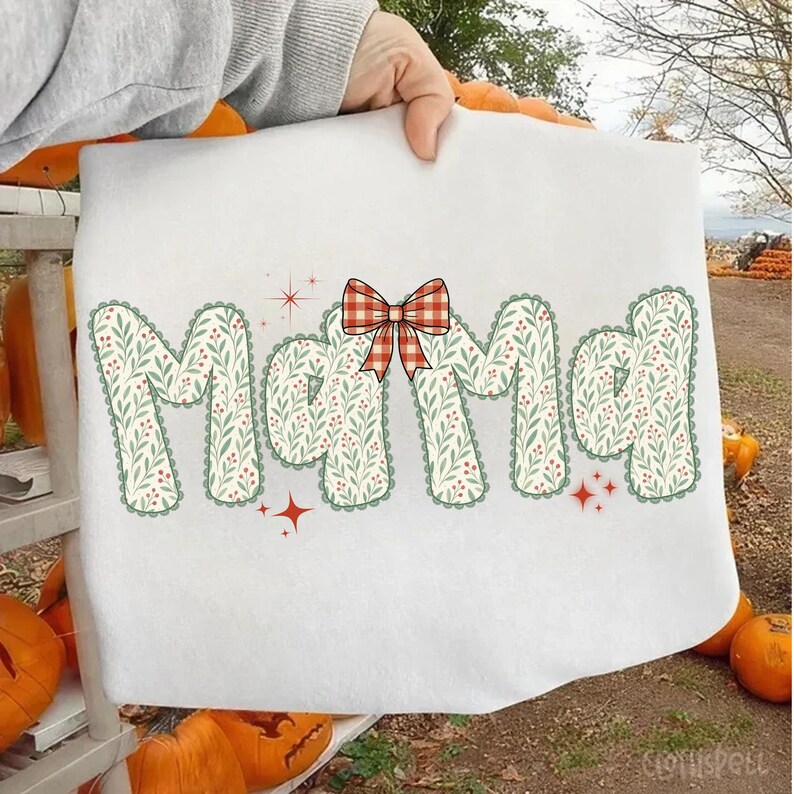 Pode incluir: Toalha decorativa branca com a palavra "Mama" em um design floral com um la&ccedil;o xadrez vermelho e branco. As letras s&atilde;o preenchidas com um padr&atilde;o floral verde e branco e contornadas em verde. Acentos de estrelas vermelhas tamb&eacute;m est&atilde;o inclu&iacute;dos.