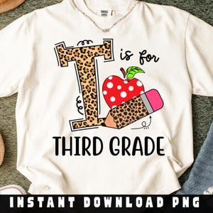 May include: Cream-colored t-shirt with a graphic design for third grade. The design includes a leopard print letter "T", a red apple with white polka dots, and a pencil. The words "Third Grade" are printed in black.