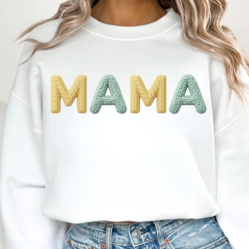 Op de afbeelding: Witte sweatshirt met het woord "MAMA" in getextureerde, 3D-letters. De letters "M" en "A" zijn geel, terwijl de middelste "A" lichtblauw is. De sweatshirt heeft een casual stijl.