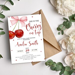 K&ouml;nnte beinhalten: Eine wei&szlig;e Babyparty-Einladung mit einer rosa Schleife und zwei roten Kirschen. Der Text lautet "She is the Cherry on Top" und "Amelia Smith".