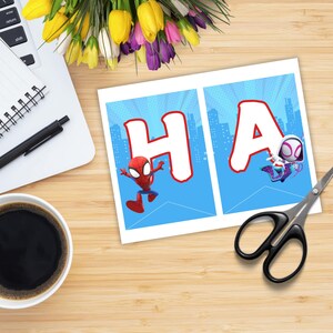 Puede incluir: Un bander&iacute;n con las letras "HA" en blanco con contornos rojos, con los personajes de Spider-Man y Spider-Gwen sobre un fondo azul con un horizonte urbano. Sobre una superficie de madera con una taza de caf&eacute;, un bol&iacute;grafo y tijeras.