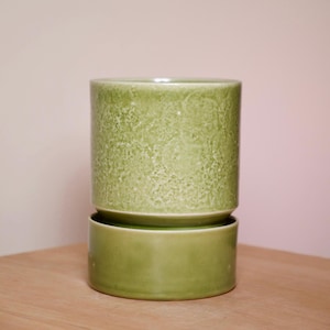 May include: A green ceramic planter with a textured finish and a matching saucer. The planter has a slightly flared lip and a smooth, rounded base.
