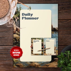 May include: A notepad set with three designs. The main notepad has "Daily Planner" text. Two smaller notepads are labeled "Shopping List" and "Notes". A red seal reads "Set of 3 Notepad Designs". The background features a coastal landscape.