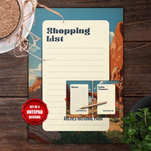 May include: A set of three notepad designs featuring illustrations of Arches National Park. The main notepad has the words "Shopping List" at the top. The set includes a "Notes" pad and a "Daily Planner" pad. The set is on a wooden surface.