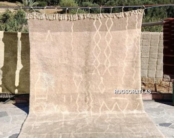Könnte beinhalten: Beiger Teppich mit geometrischem Rautenmuster und Fransen, der im Freien ausgestellt ist. Der Teppich hängt an einer Metallstange mit anderen Teppichen im Hintergrund. Der Text "RUGSORATLAS" ist sichtbar.