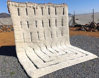 Puede incluir: Una alfombra blanca y negra con estampado geométrico y borde de flecos. La alfombra está doblada por la mitad y está sobre una superficie de grava.