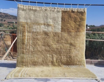 Op de afbeelding: Een handgeweven beige en bruin kleed met een geometrisch patroon. Het kleed hangt aan een waslijn buiten.