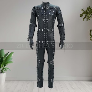 May include: A black leather jumpsuit with multiple straps, buckles, and metal ring accents. The long-sleeved garment features a high collar, front closure, and is paired with black gloves. The text "ZR Leather Studio" is visible.