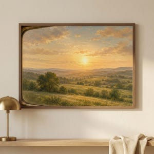 Può includere: Un dipinto di paesaggio incorniciato raffigura un tramonto su dolci colline e campi verdi. Il cielo è pieno di tonalità dorate e arancioni, con un sole luminoso in lontananza. L'opera d'arte è in una cornice di legno.