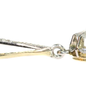May include: A silver and gold pendant with a large, clear gemstone set in a prong setting. The pendant has a bail that is attached to a chain.
