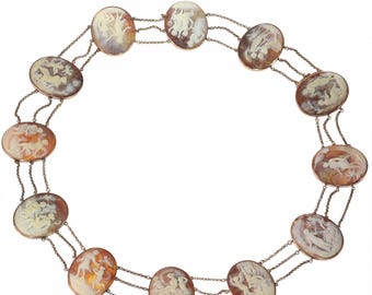 May include: A necklace featuring oval cameo pendants with classical relief carvings. The cameos are set in gold-toned frames and connected by delicate silver chains. The carvings depict figures in shades of white, brown, and orange.