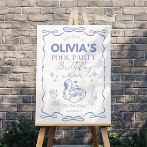 Può includere: Un cartello bianco su un cavalletto di legno con la scritta "Benvenuti alla festa in piscina di Olivia". Il cartello ha un bordo blu e illustrazioni di un galleggiante a forma di cigno, cocktail e un carrello per la piscina. Lo sfondo è un muro di mattoni.