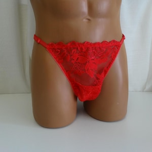 May include: Red lace underwear with a delicate floral pattern. The thong-style underwear features a scalloped edge along the waistline and thin straps. The lingerie is displayed on a mannequin.