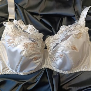 Op de afbeelding: Een witte satijnen bh met ingewikkelde kanten details en delicate bloemenborduursels. De bh heeft verstelbare bandjes en een klassiek ontwerp. Het is een lingerie-artikel.