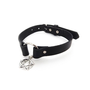 May include: Black leather choker necklace with a silver-colored pentagram pendant. The choker has a metal ring and adjustable buckle closure. The necklace is on a white background.