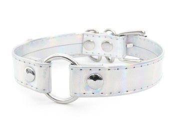 May include: A silver choker with a large silver ring and multiple silver studs. The choker has a holographic finish.