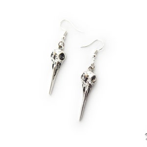 Puede incluir: Un par de pendientes de plata con un diseño detallado de cráneo de pájaro. Los pendientes son de estilo colgante con cierre de gancho.