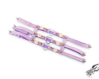 May include: Three lavender-colored, decorative harnesses with silver spikes, heart-shaped accents, and small pink rose embellishments. The harnesses are made of a soft fabric and are designed to be worn on the body.