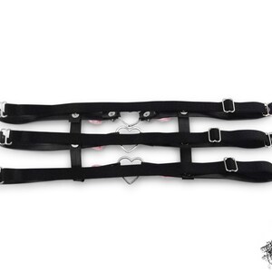 Rear view of a black thigh garter showing 3 black satin elastic straps with adjustable sliders for a comfortable and versatile fit. Design features silver heart rings, pink satin roses and silver spike studs for an edgy yet kawaii look. Perfect for alternative fashion styles including pastel goth, Harajuku fashion and coquette aesthetics, as well as cosplay and BDSM communities. Displayed on a white background.