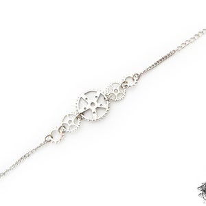 May include: A silver chain bracelet featuring a series of interlocking gears as a decorative element.