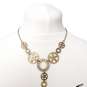 Unique handmade Steampunk necklace featuring intricately detailed bronze-tone gears and cogs. Suspended on a white mannequin bust, this bold necklace highlights its intricate links and clockwork inspired design. This handmade necklace showcases a vintage industrial aesthetic, perfect for steampunk enthusiasts and mechanical-inspired fashion lovers