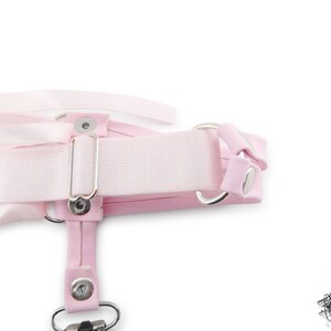 Rear view of a pink corset lacing thigh garter, showing the stretchy pink elastic strap with slider adjustment, ensuring a comfortable and versatile fit. Perfect for pastel goth, kawaii and Japanese fashion lovers, this pink thigh garter makes a bold addition to alternative fashion wardrobes. It is also an alternative option for bridal garters and alternative weddings, making a bold and unique statement on your special day. Photographed on a white background.