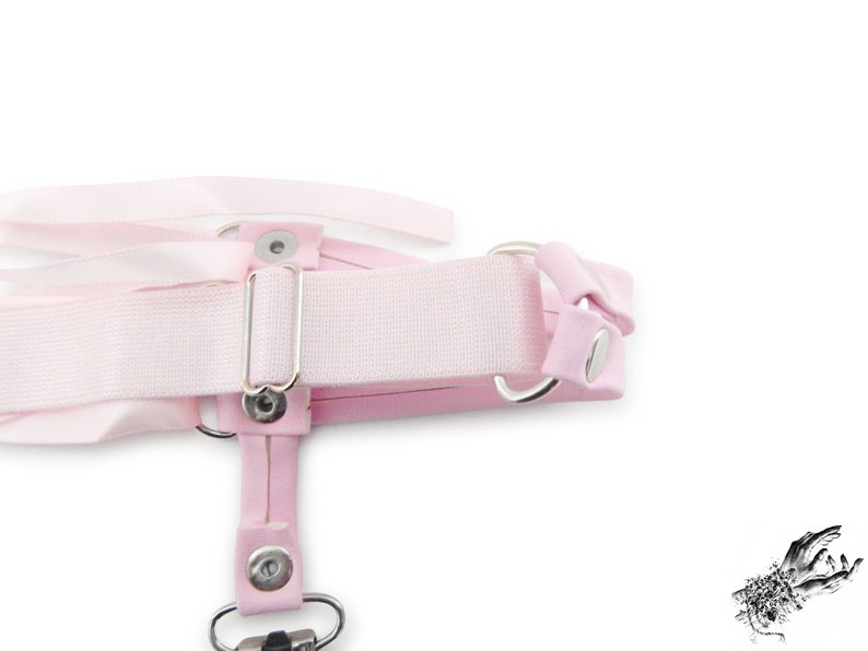 Rear view of a pink corset lacing thigh garter, showing the stretchy pink elastic strap with slider adjustment, ensuring a comfortable and versatile fit. Perfect for pastel goth, kawaii and Japanese fashion lovers, this pink thigh garter makes a bold addition to alternative fashion wardrobes. It is also an alternative option for bridal garters and alternative weddings, making a bold and unique statement on your special day. Photographed on a white background.