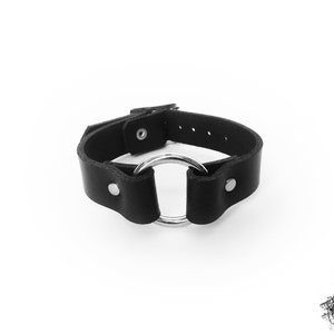 Black leather wristband with a silver O ring in the center, and two silver coloured flat shaped rivets holding the black leather and O ring in place. There is a silver buckle at the back with multiple holes to fit 16cm to 21cm wrist circumference.