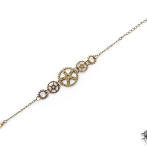 Peut inclure: Un bracelet doré avec une chaîne et plusieurs breloques en forme d'engrenages.